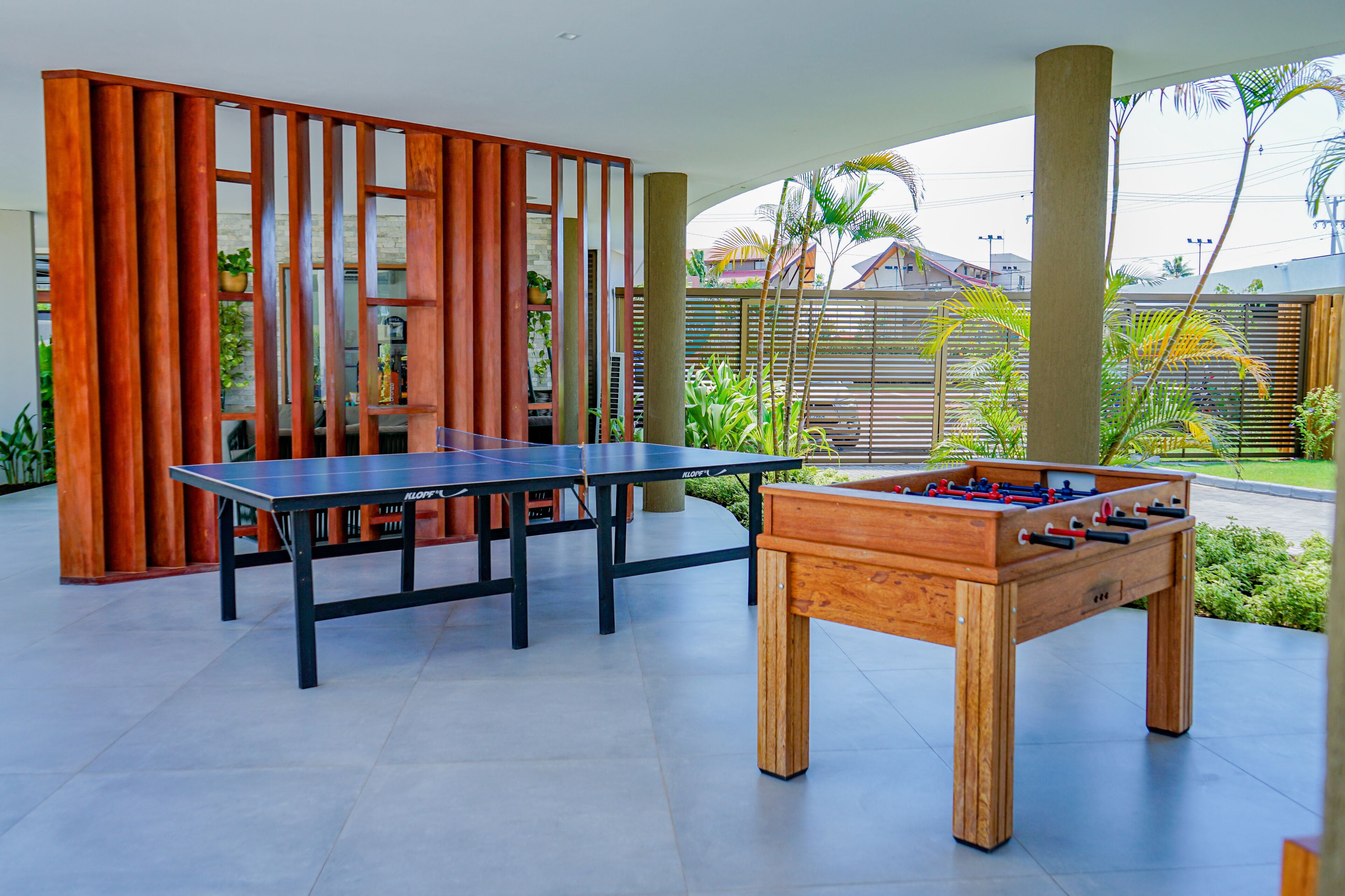 A modern indoor recreational area with a foosball table and a ping pong table, surrounded by wooden partitions and plants.