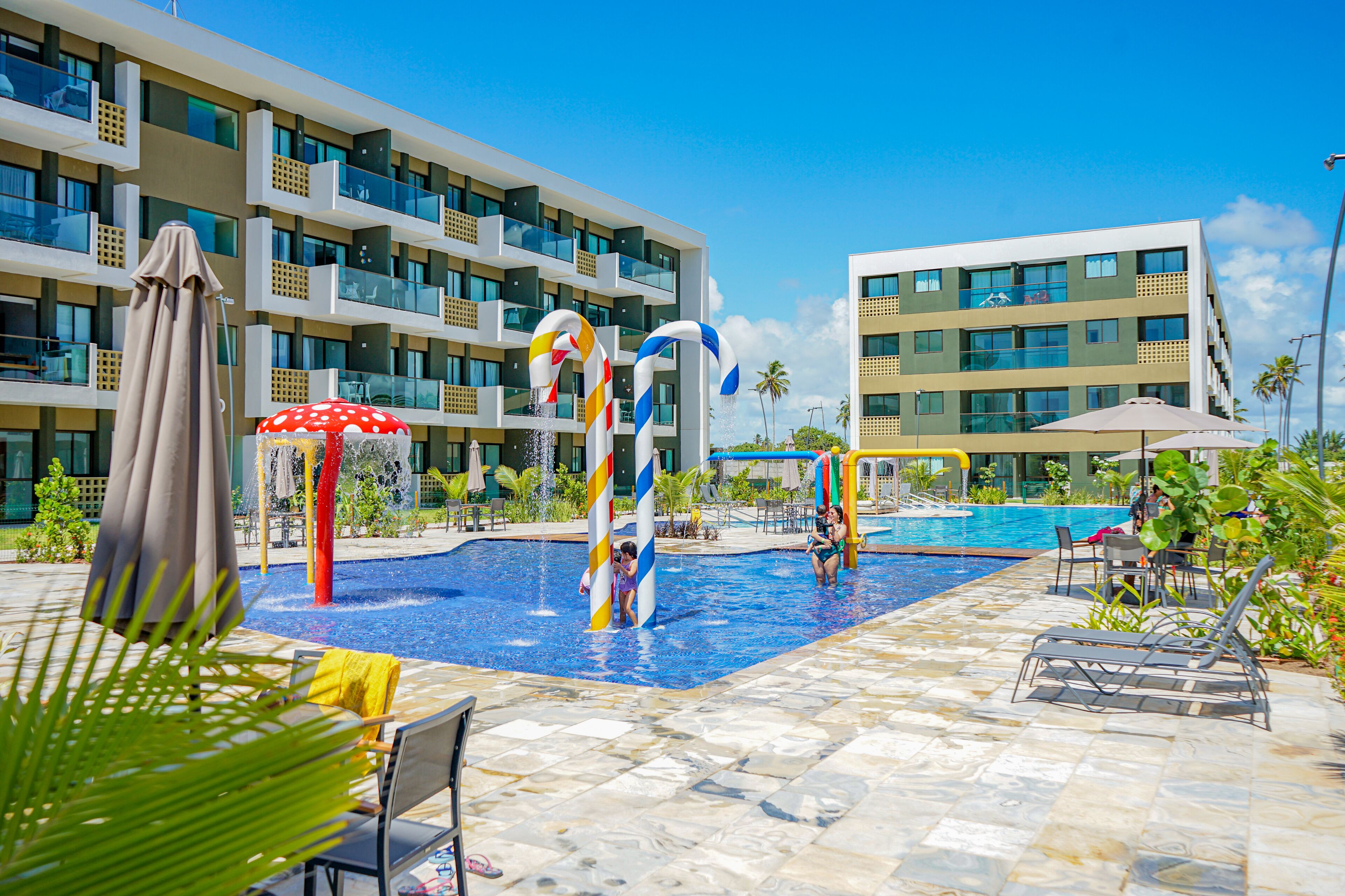 A swimming pool area with lounge chairs and umbrellas, surrounded by a multi-story hotel building.