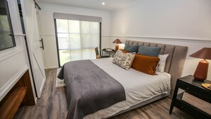 A modern bedroom with a large bed, a nightstand, a lamp, and a view of the outdoors through a sliding door. - LUMLEY ABODE : Bright (Bright)