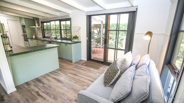 A modern kitchen with a central island, a dining area with a sofa and cushions, and large sliding glass doors leading to an outdoor patio. - LUMLEY ABODE : Bright (Bright)
