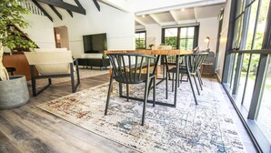 A modern dining area with a wooden table and black chairs, a large window with a view, and a TV mounted on the wall. - LUMLEY ABODE : Bright (Bright)