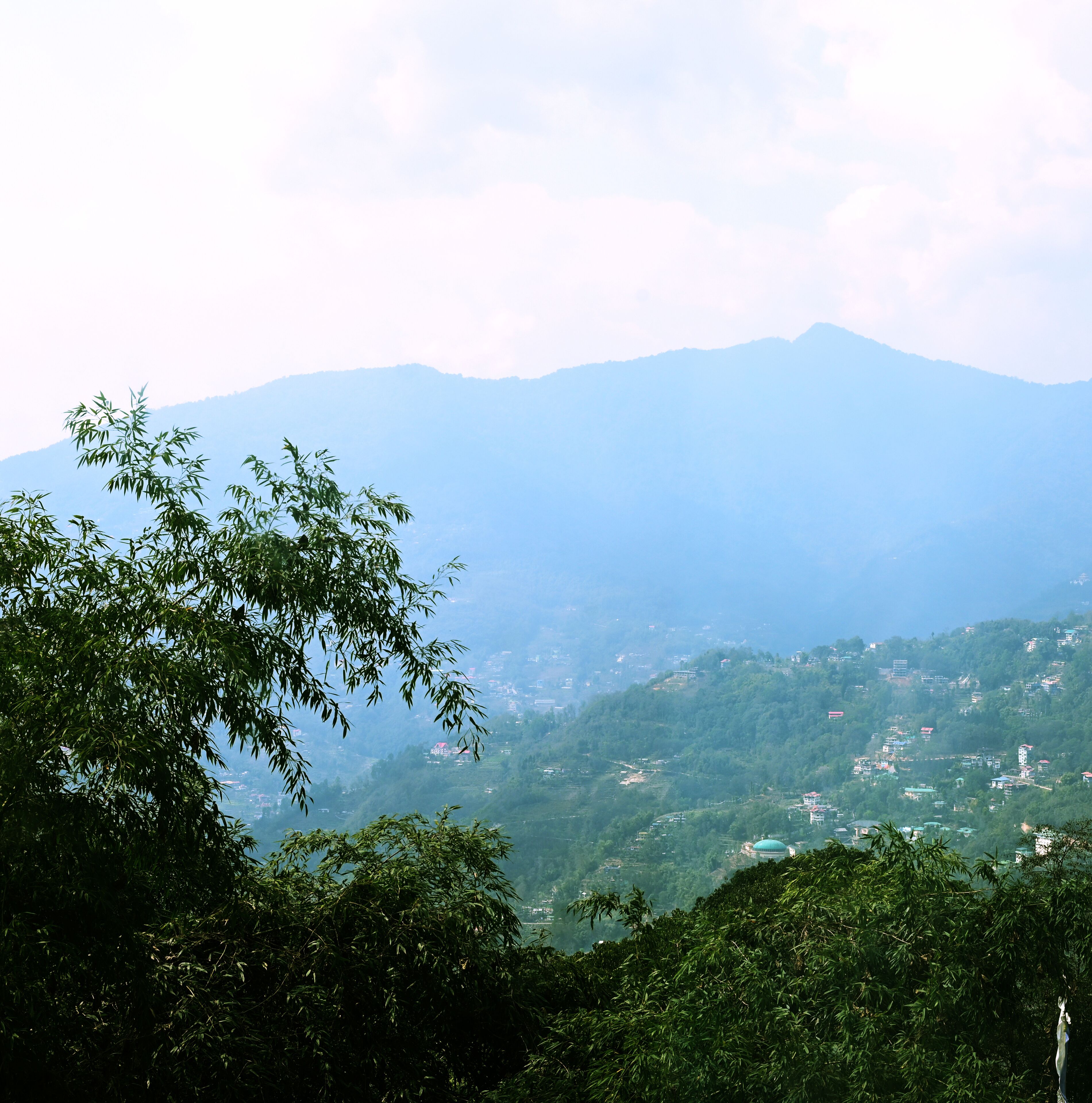 A mountainous landscape with dense greenery and scattered buildings.
