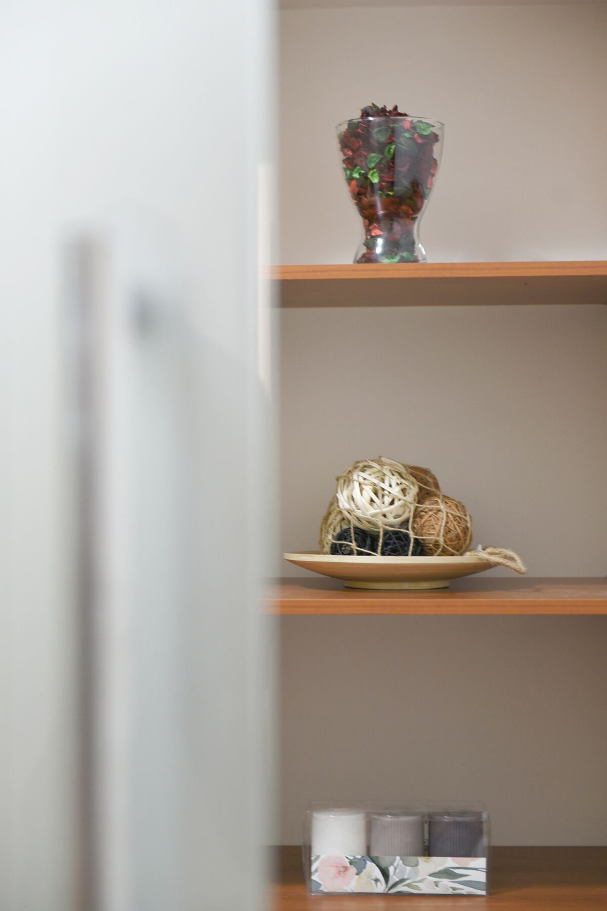 Uma prateleira com objetos decorativos, incluindo um vaso de vidro, uma cesta de palha e uma caixa com motivos florais.