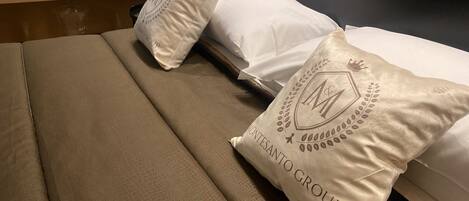 A hotel room with a bed featuring white linens and two decorative pillows with the logo "MONTESANTO GROUP".