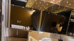 A modern bathroom with a large mirror, a sink, and a vanity. There are towels and a vase on the vanity. - Montesanto Group  (Naples)