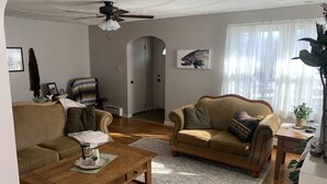 A living room with two sofas, a wooden coffee table, a ceiling fan, and a large window with sheer curtains. - Conneaut Creek Cottage (Conneaut)