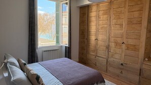 Une chambre à coucher avec un lit, une fenêtre avec des rideaux, une armoire en bois et un luminaire suspendu.