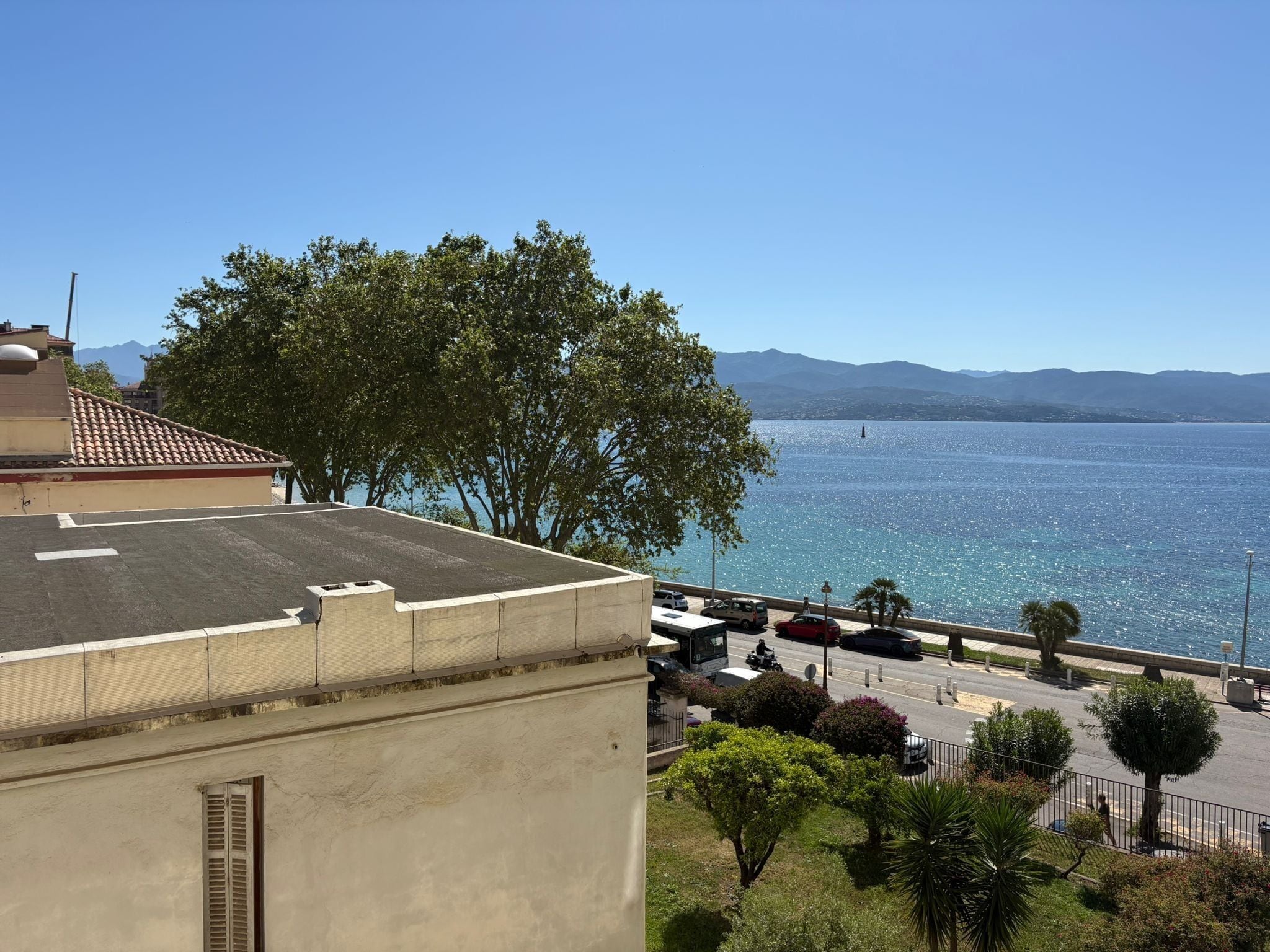 Vista sulla costa con un edificio, alberi e cielo sereno.
