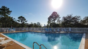 A swimming pool with a wooden deck, metal pool ladder, and white poolside chairs.