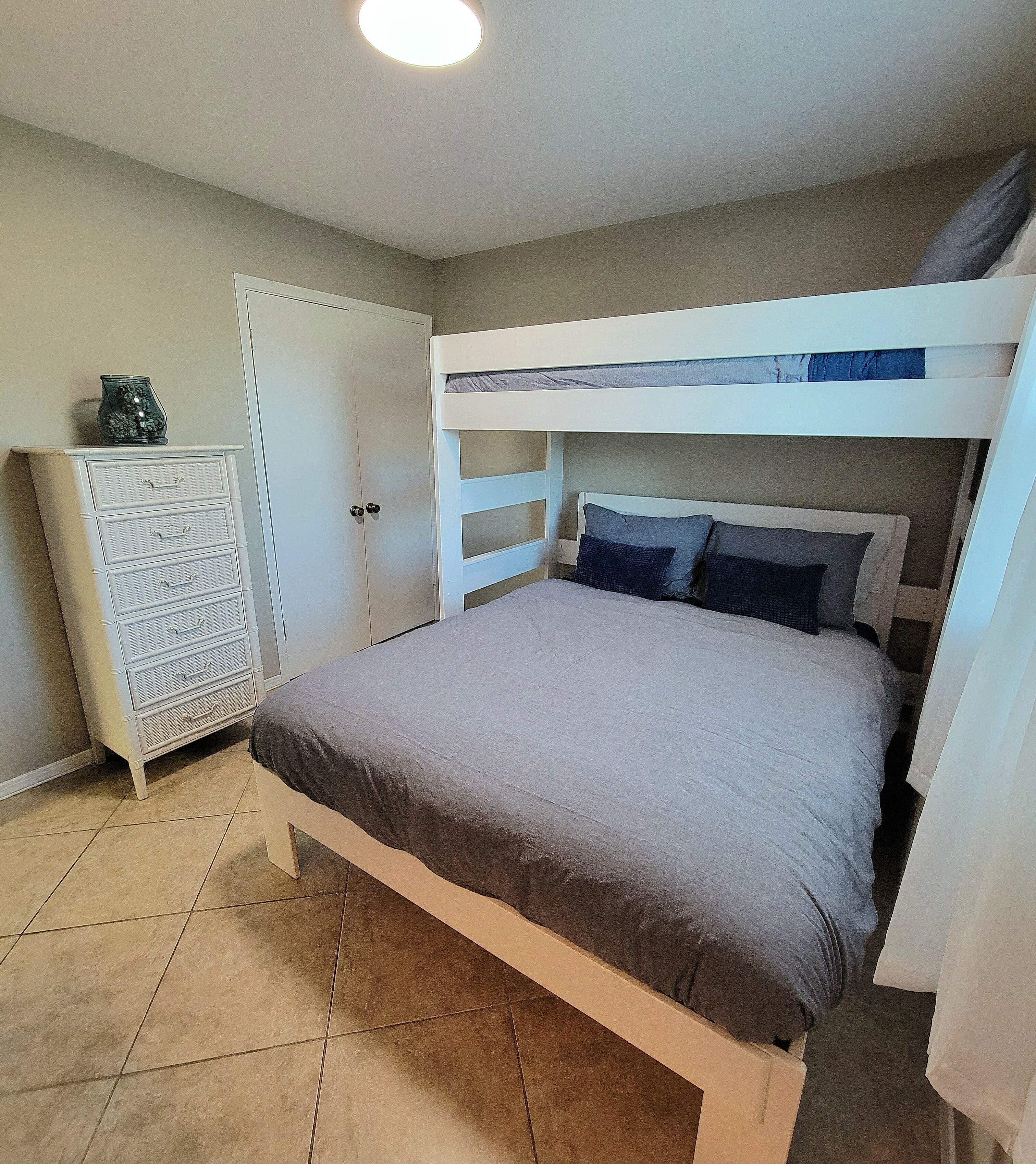 A bunk bed with a grey mattress and pillows, a white dresser with drawers, and a door with a keyhole.
