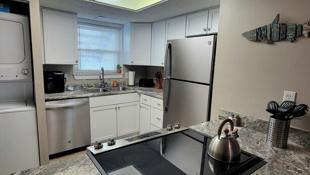 A modern kitchen with white cabinets, a stainless steel refrigerator, a black induction cooktop, and a skylight above.