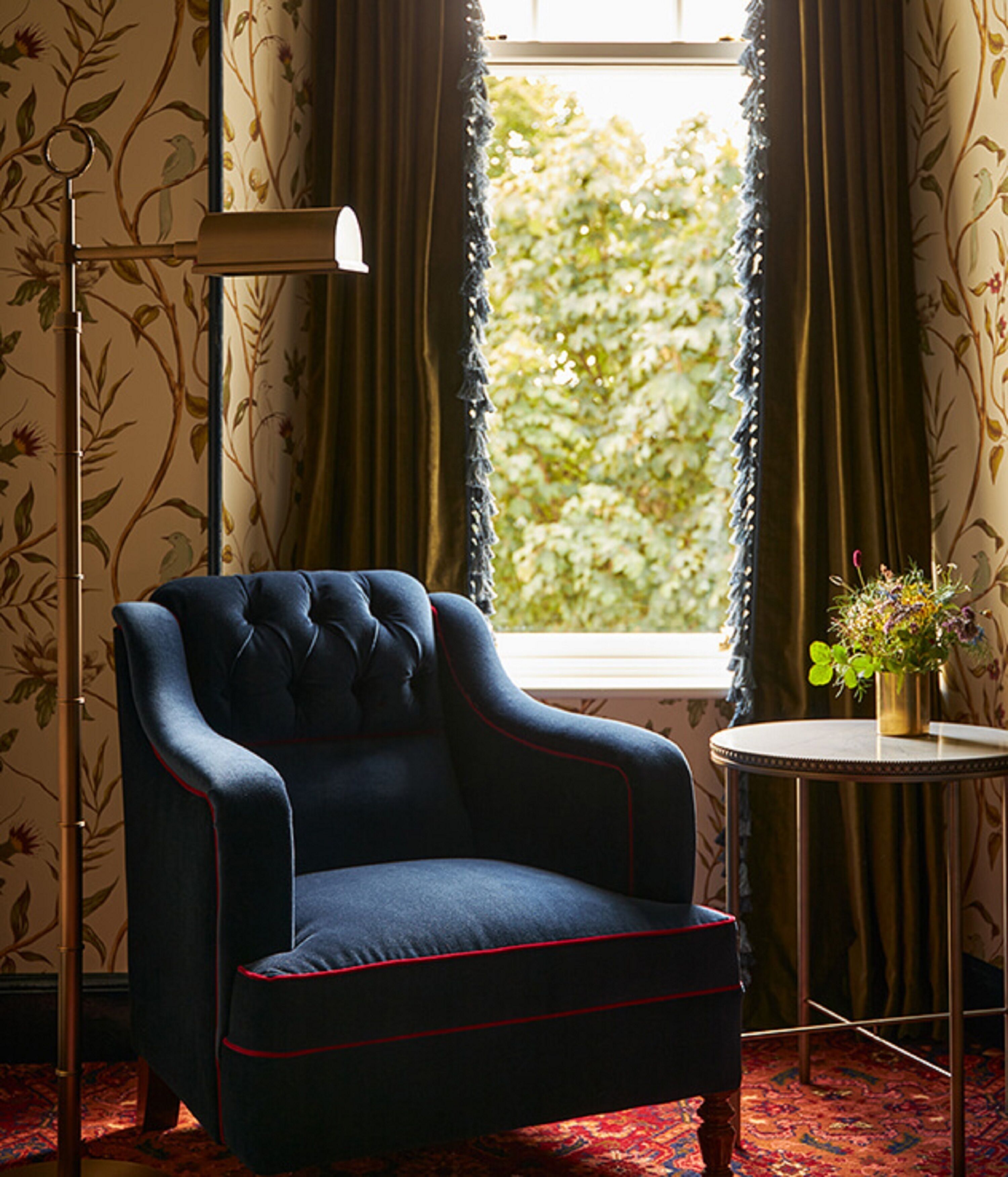 A dark blue armchair with red piping, positioned next to a floor lamp and a small table with a vase of flowers.
