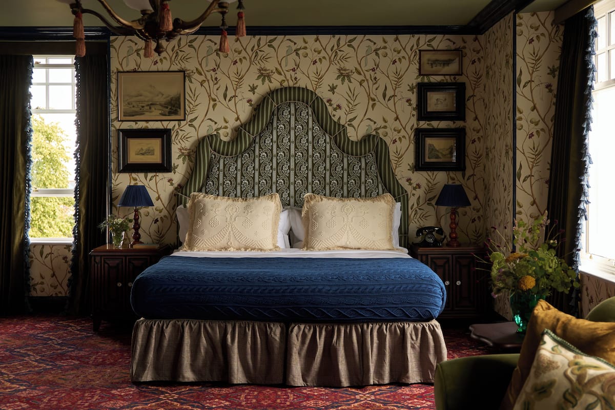 Une chambre avec un grand lit, un papier peint à motifs floraux et des tableaux encadrés accrochés au mur.