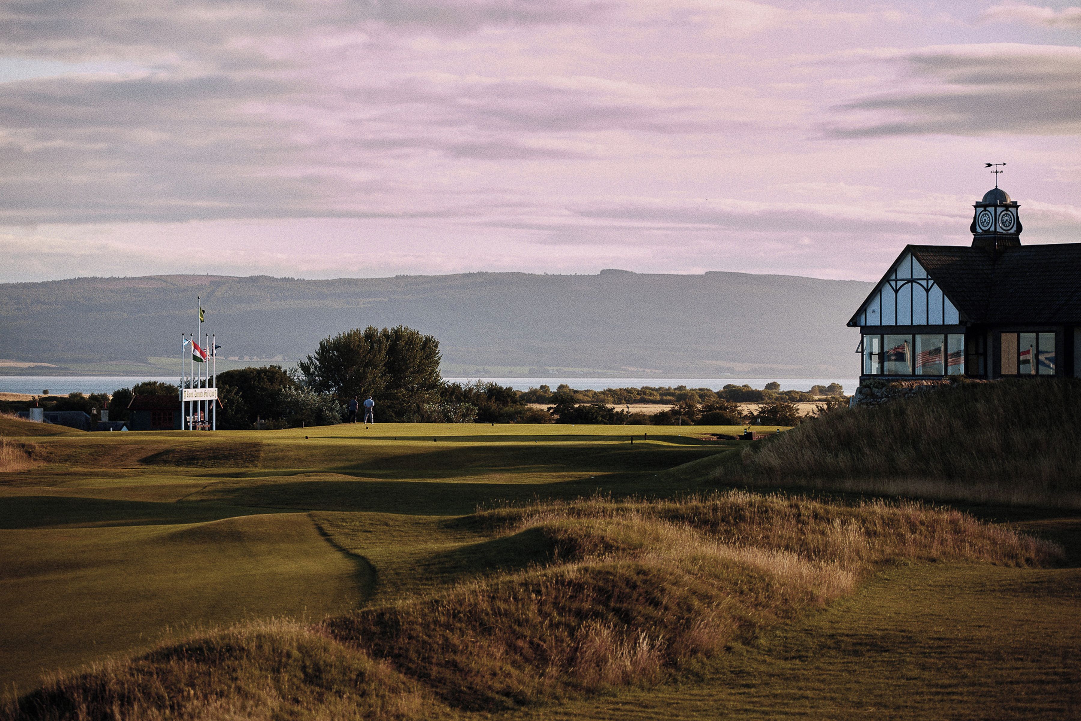 A golf course with a clubhouse, a flagpole, and a view of the sea.