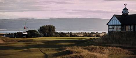 A golf course with a clubhouse, a flagpole, and a view of the sea.
