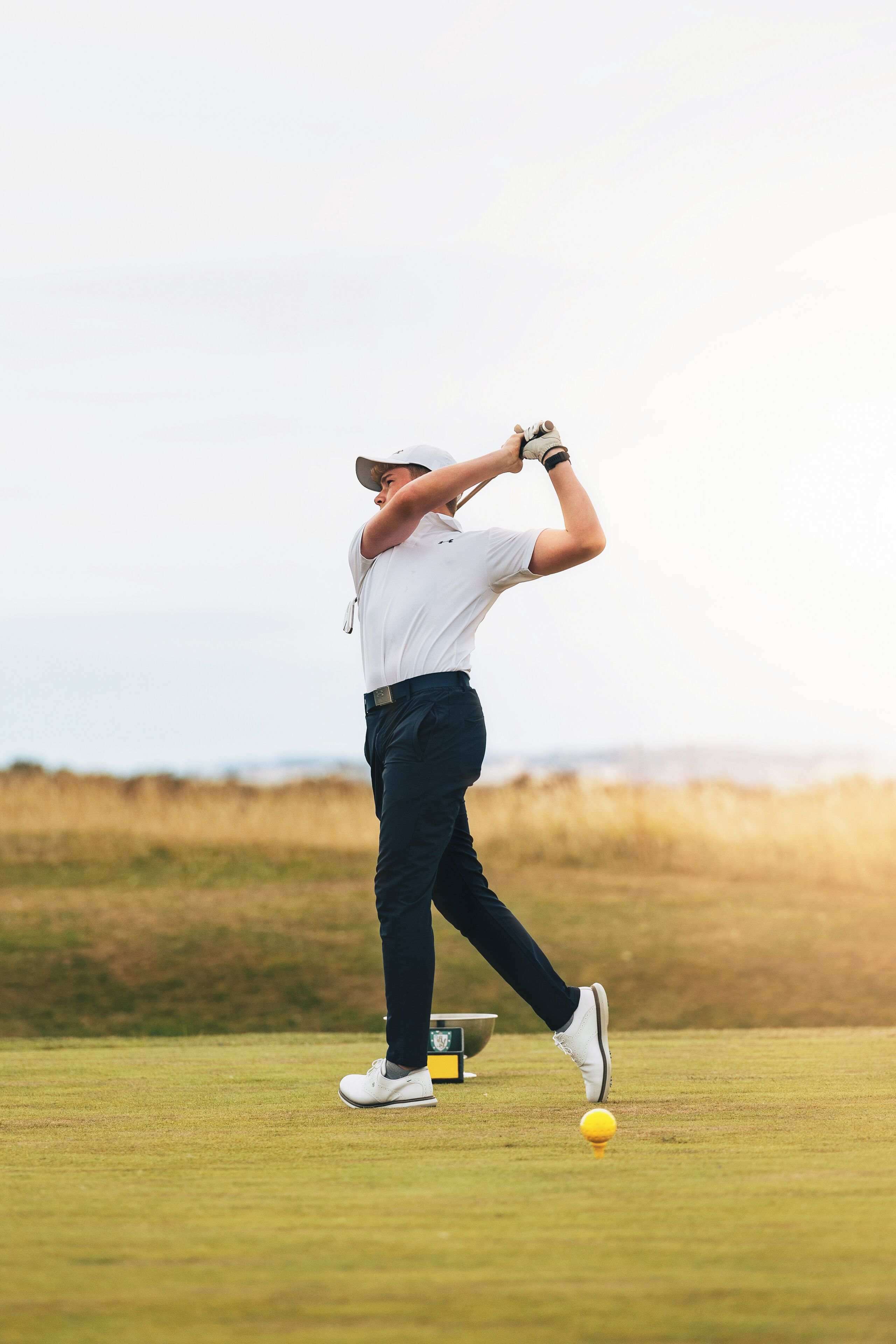 A person playing golf, wearing a white shirt and dark pants, with a golf club in hand.