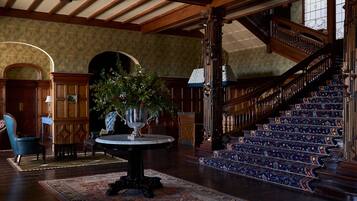 A grand staircase with ornate railings, a round table with a vase of flowers, and a patterned rug on the floor.