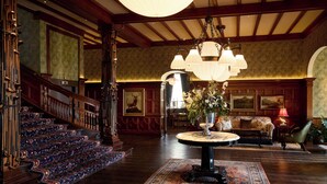 A grand lobby with a staircase, a round table with a vase, and a chandelier. - Dornoch Station (Dornoch)