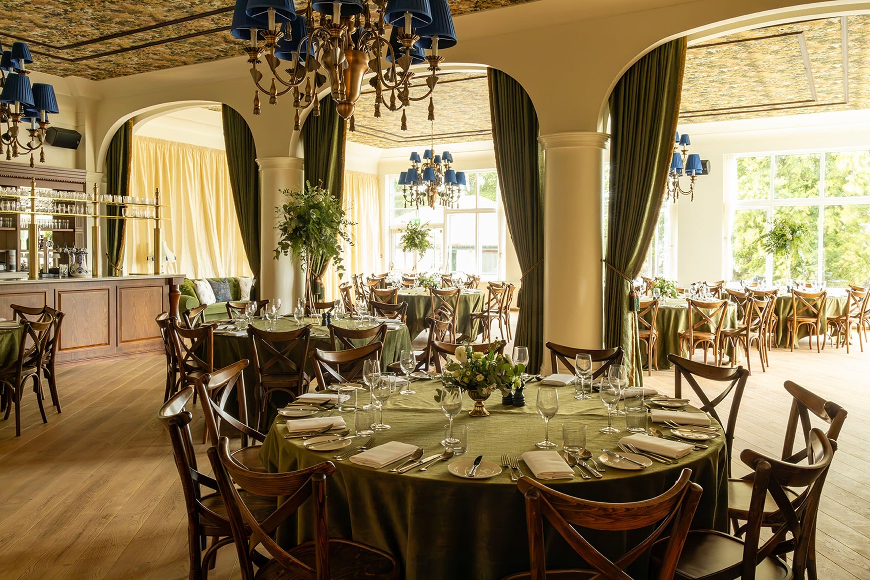 A formal dining room with round tables, wooden chairs, and chandeliers.