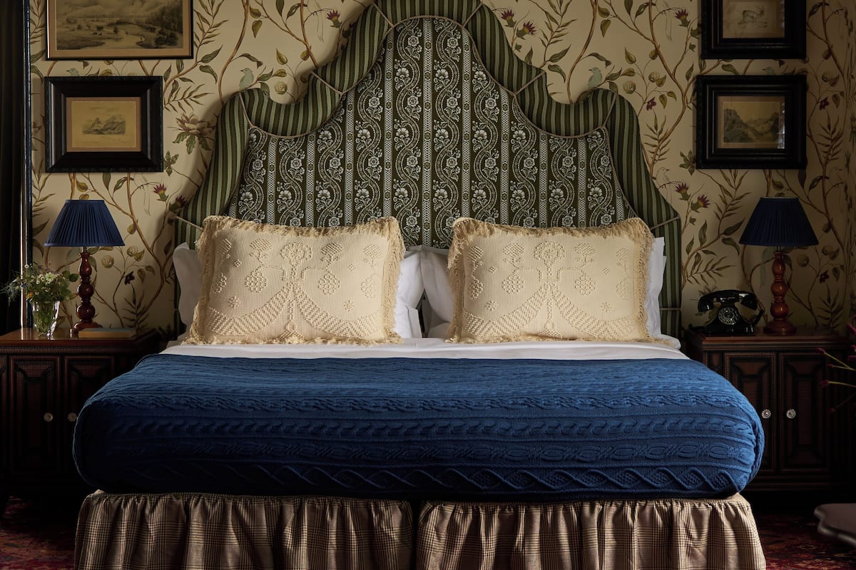 Un lit avec une tête de lit verte, deux oreillers, une couvre-lit bleue et un tapis rouge à motifs.