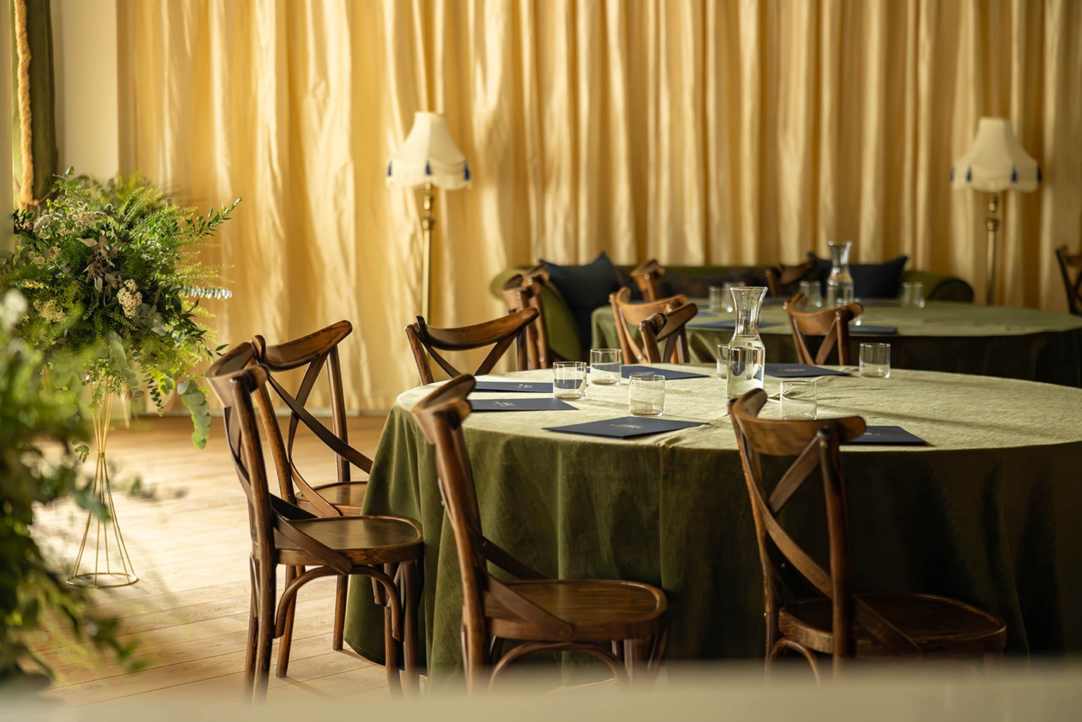 Un comedor con mesas redondas, sillas de madera y manteles verdes.