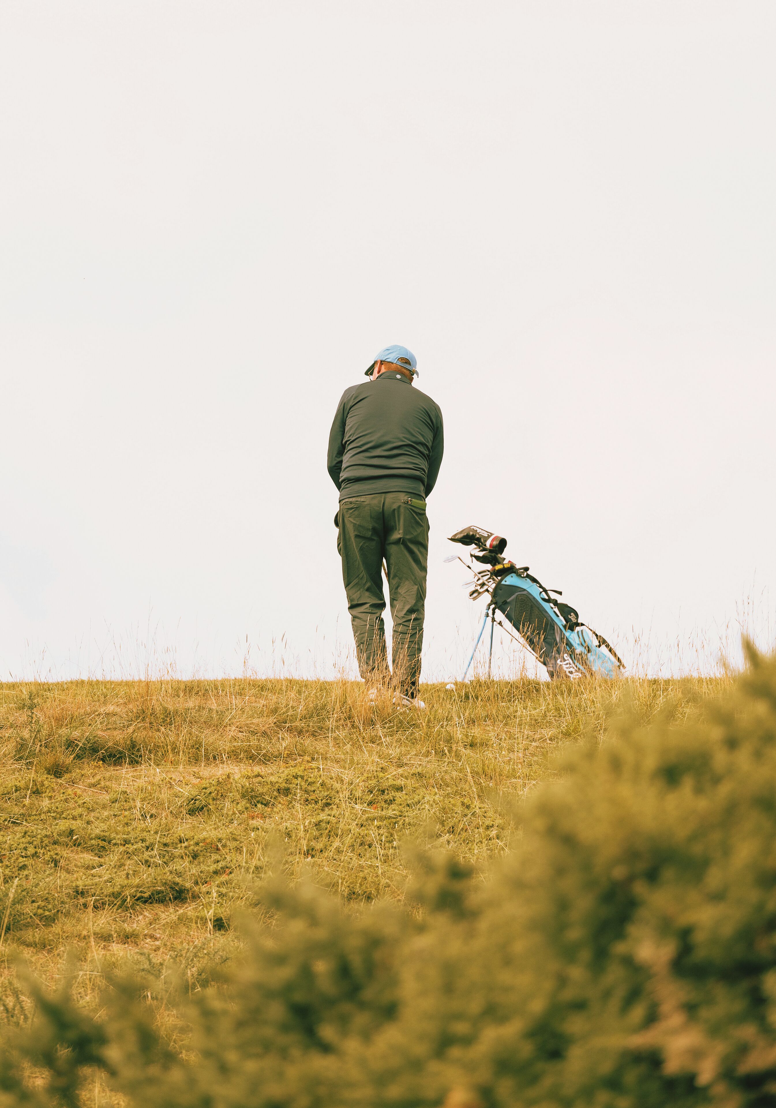 A person standing on a grassy hill with a camera on a tripod.