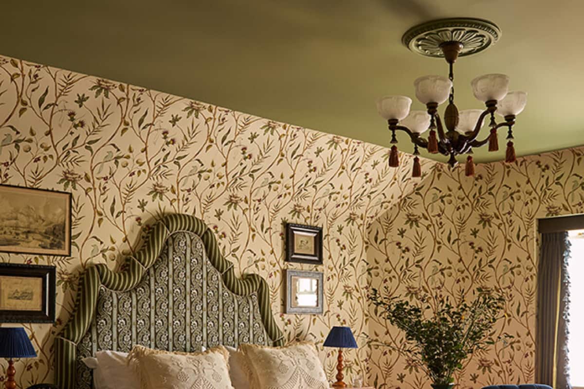Une chambre à coucher avec un grand lit, deux fauteuils, une table, un lustre et un papier peint à motifs.
