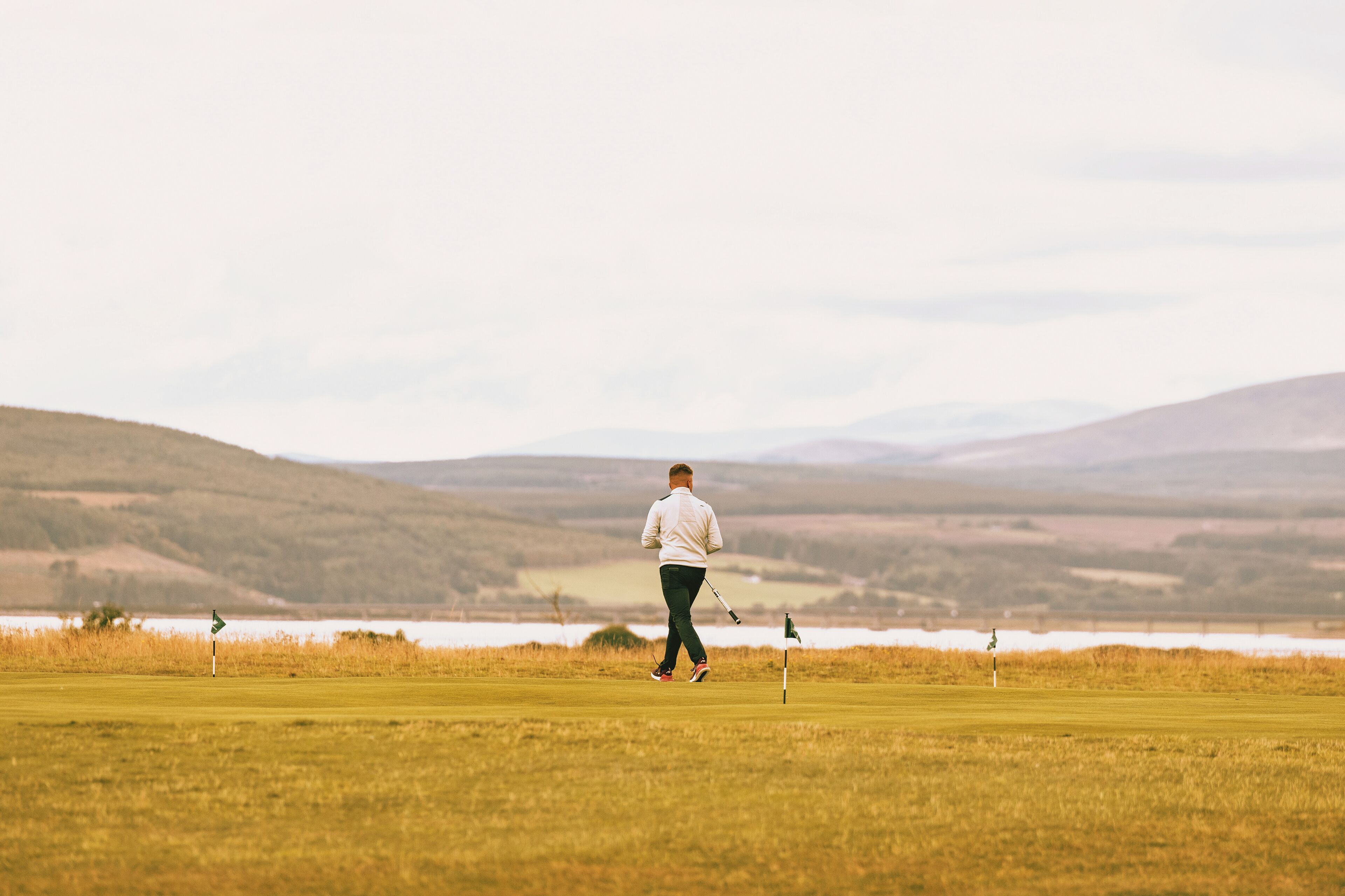A person walking on a golf course with a flagstick in the distance.