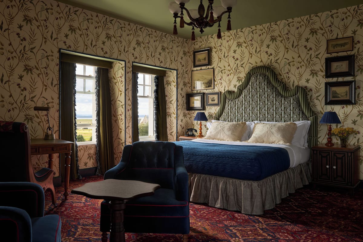 Une chambre à coucher avec un grand lit, un bureau, une chaise et une vue par la fenêtre.