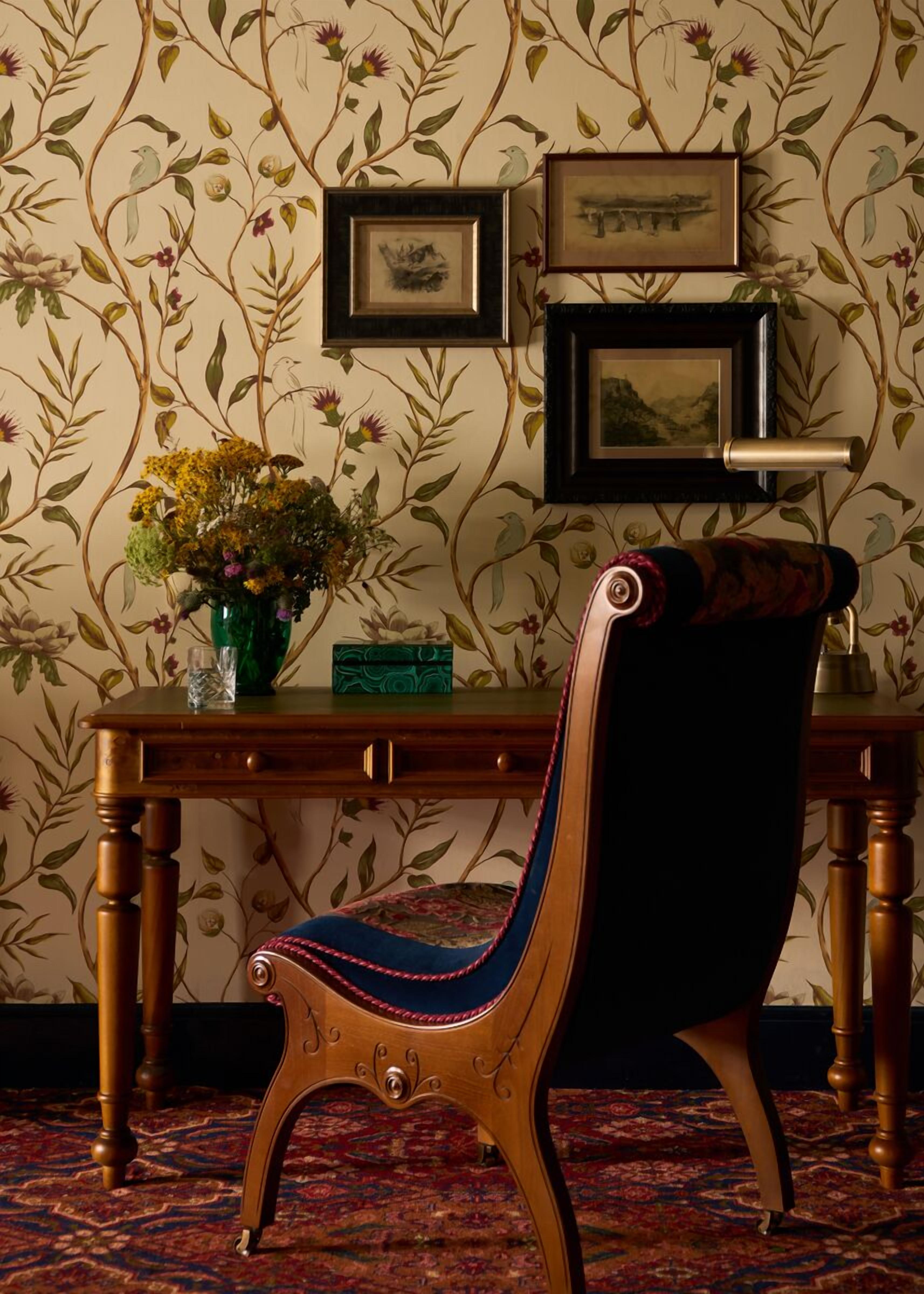 Une pièce avec une chaise en bois, une table ornée d’un vase de fleurs et des tableaux encadr és accrochés au mur.
