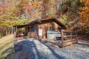 Situated in a forested area, this cabin features a porch with a railing and a hot tub.