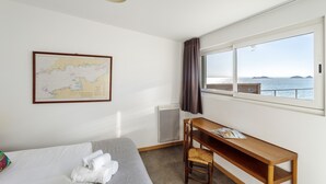Habitación de hotel con cama, un escritorio de madera, una silla, un mapa en la pared y ventana con vista al mar.