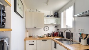 Una cocina moderna con armarios blancos, encimera de madera, un lavamanos, una cafetera, un tostador y un reloj.