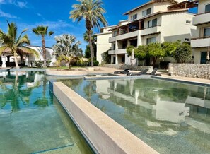 A swimming pool with lounge chairs, palm trees, and a multi-story building with balconies. - Casas TMar (Cabo San Lucas)
