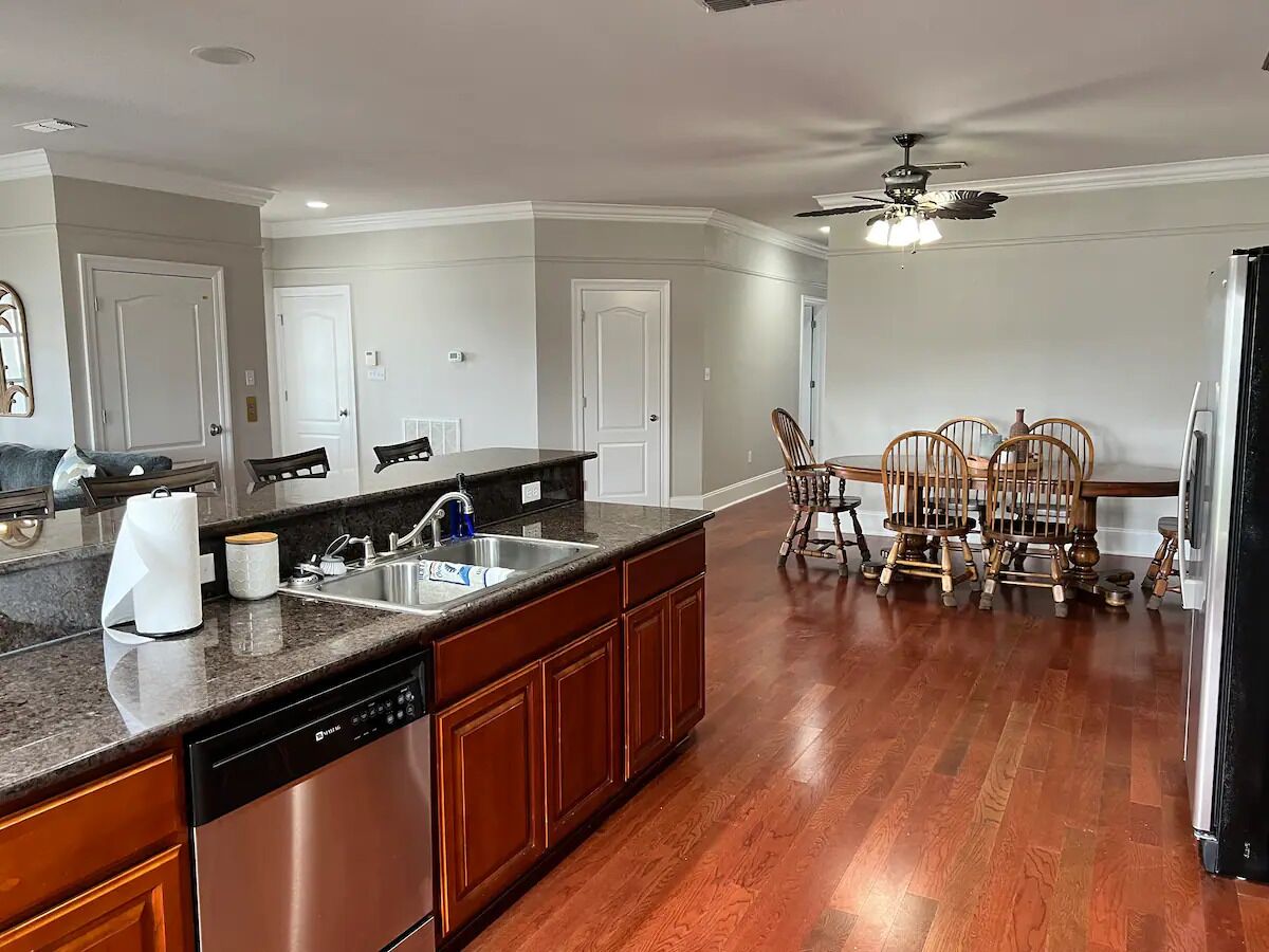 A kitchen with a dishwasher, a sink, and a dining area with wooden chairs.