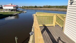 Een houten terras met uitzicht op een kalme waterpartij, met een klein steiger en een gebouw op de achtergrond.