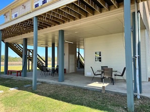 An outdoor covered patio area with a table and chairs, a staircase leading to an upper level, and a door to the side. - Waterfront Paradise (Bay St. Louis)