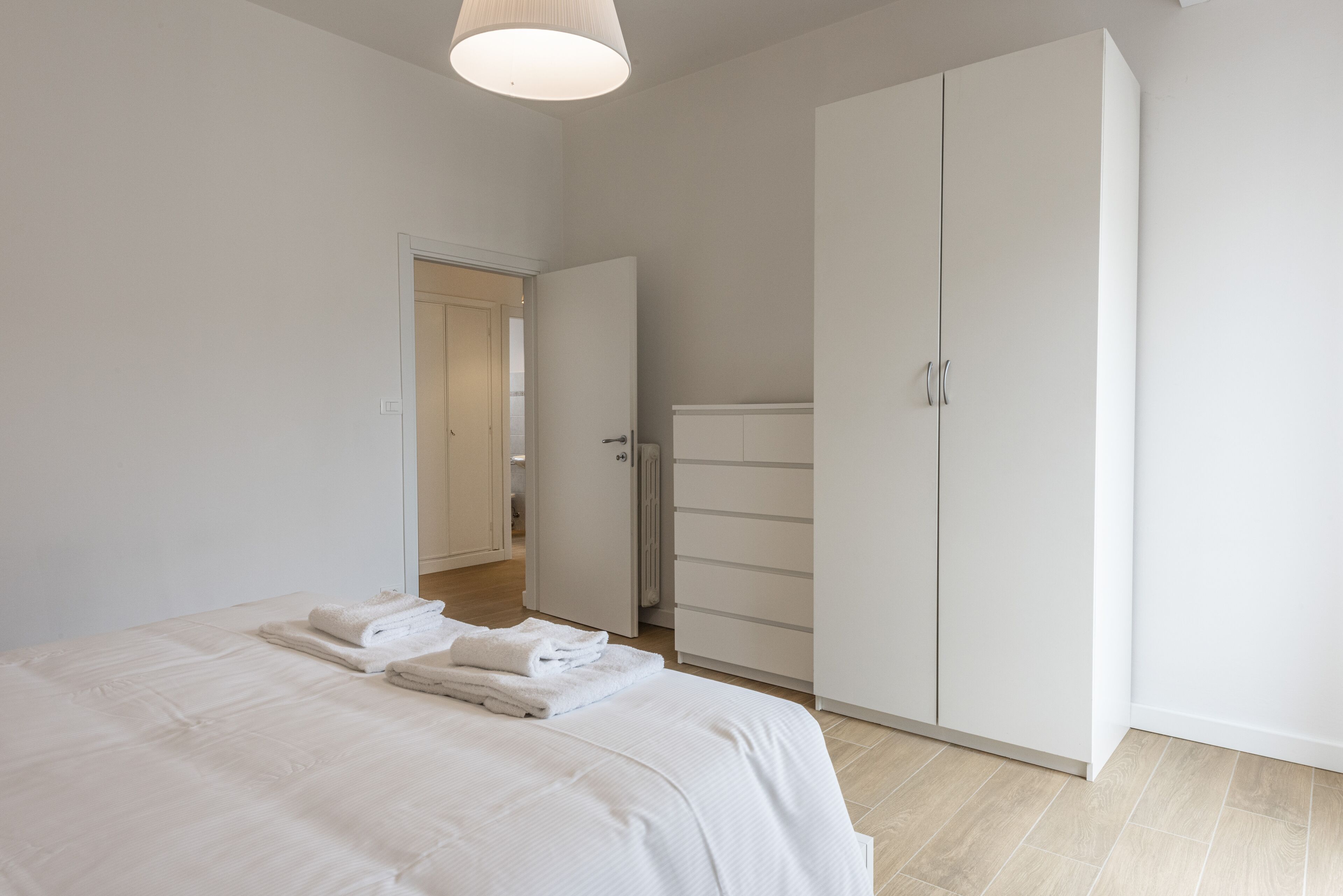 A bedroom with a large bed, a wardrobe, and a door leading to another room.