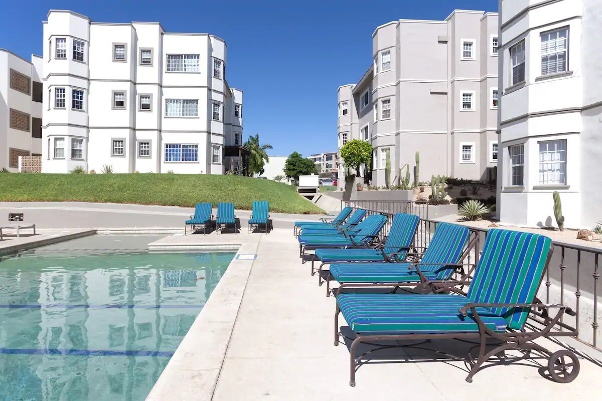Area piscina con sedie a sdraio e piscina, circondata da edifici a più piani con balconi.