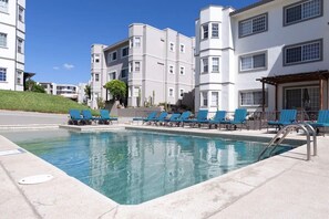 A swimming pool with blue lounge chairs, surrounded by multi-story buildings with balconies and windows. - Condos AMF (Cabo San Lucas)
