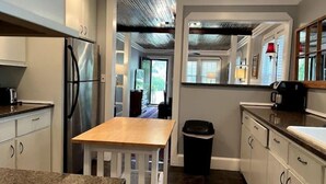 Una cocina compacta con armarios blancos, un refrigerador de acero inoxidable, una mesa de madera y un cubo de basura.