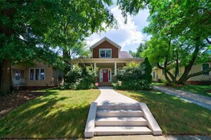 A two-story house with a front porch, a red door, and a driveway leading to the entrance. - South End Home: Pool + Spa+ Firepit+ Arcade (Charlotte)