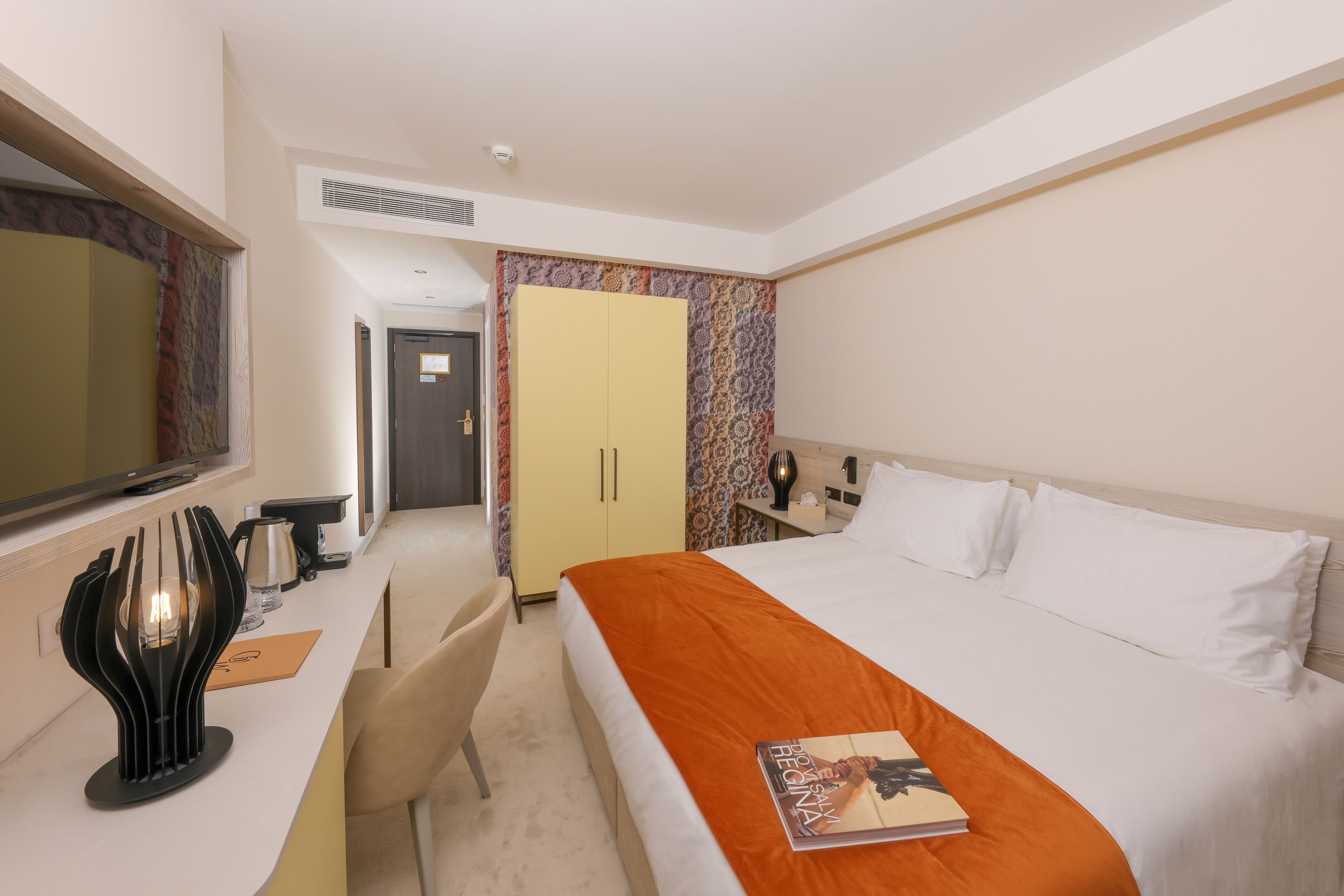 Une chambre d’hôtel avec un lit, un bureau avec une lampe, une armoire et un miroir.