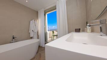 A modern bathroom with a large bathtub, a separate shower area, and a view of the outdoors through a glass door.