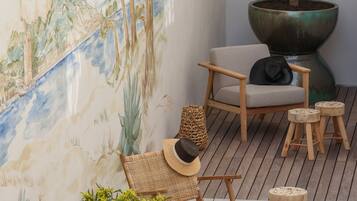 A cozy outdoor seating area with a mural, a large potted plant, and a wooden table with a glass of wine.