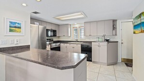 A modern kitchen with granite countertops, stainless steel appliances, and light-colored cabinetry. - Well-appointed condo on uncrowded Ormond Beach (Ormond Beach)