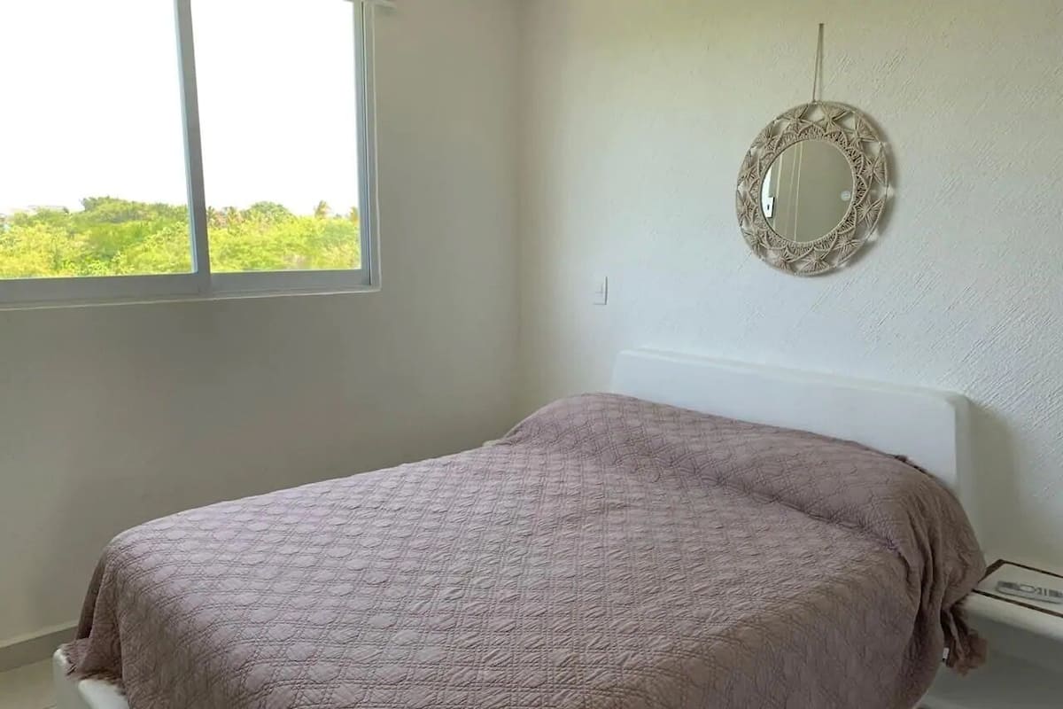 Un dormitorio con cama, ventana y espejo fijado a la pared.