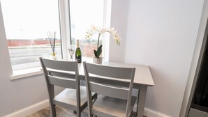 A dining area with a table and two chairs, a window with a view of a street, and a potted plant on the table. - Ferry View (Poulton-le-Fylde)