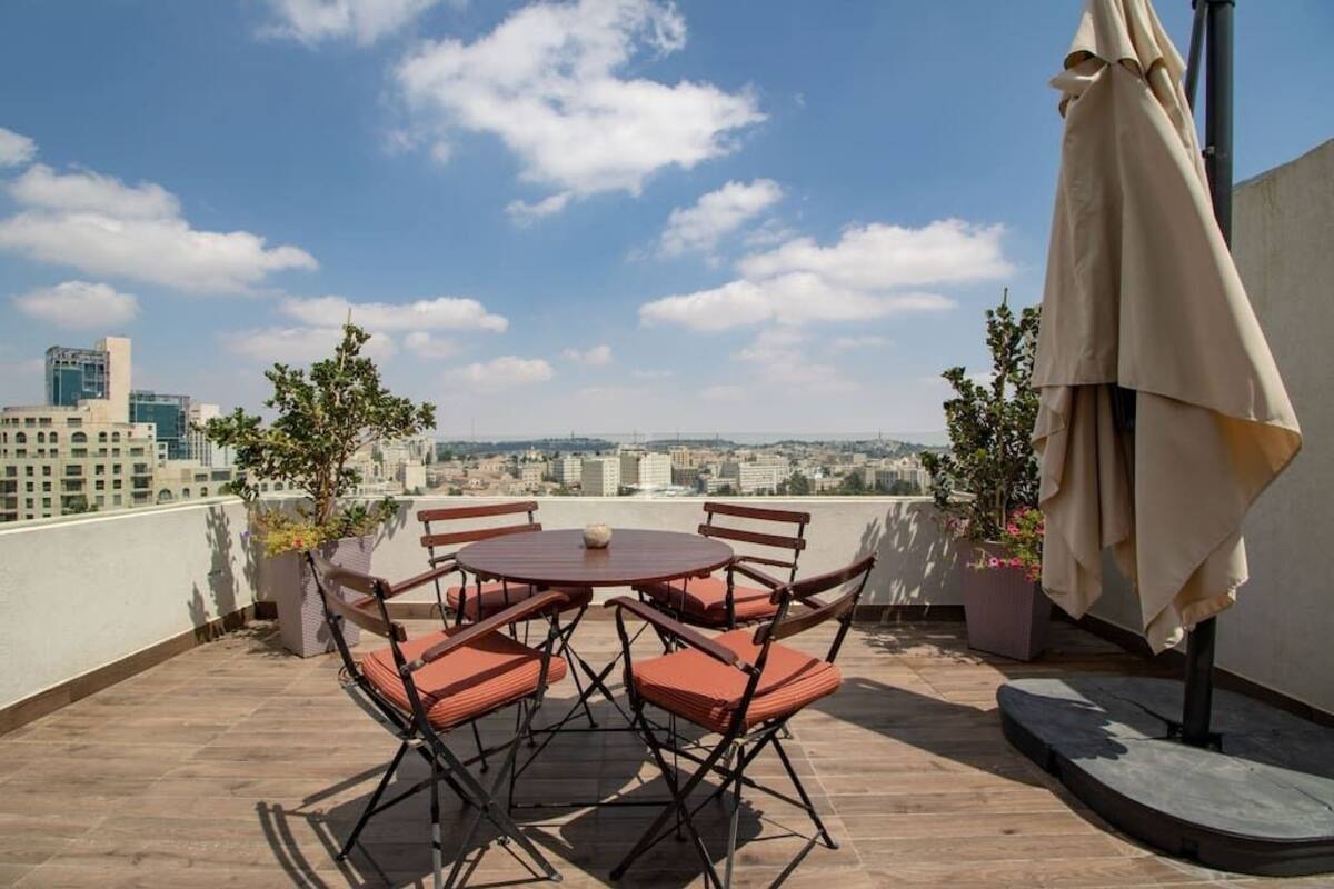 Une terrasse sur le toit, avec une table ronde et des chaises, des plantes en pot et un espace salon abrité.