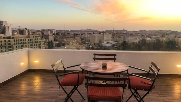 A rooftop terrace with a round table and four chairs, overlooking a cityscape at sunset. - King George Suites (Jerusalem)